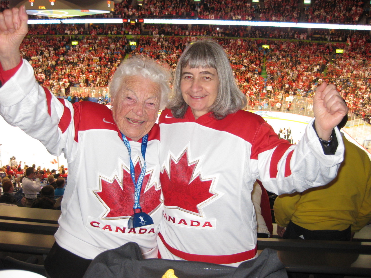Hazel McCallion in a Team Canada hockey jersey, arms raised in a packed Olympic arena.